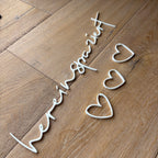 Weißer 3D-Schriftzug „hereinspaziert“ in geschwungener Schrift, liegend auf Holzoberfläche.