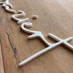 Weißes 3D-Schild „herzigziert“ aus PLA, schräg von der Holzoberfläche fotografiert.