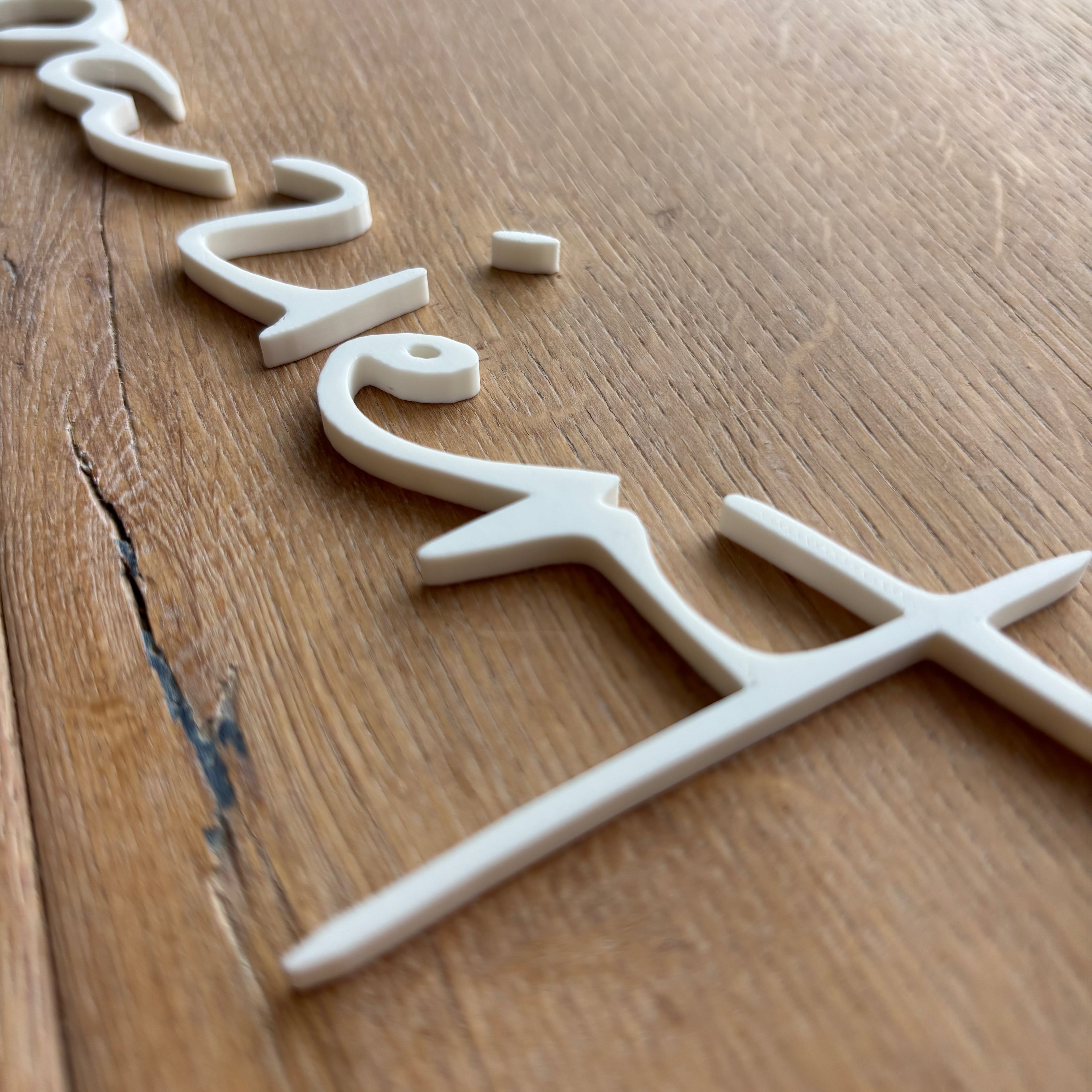 Weißes 3D-Schild „herzigziert“ aus PLA, schräg von der Holzoberfläche fotografiert.